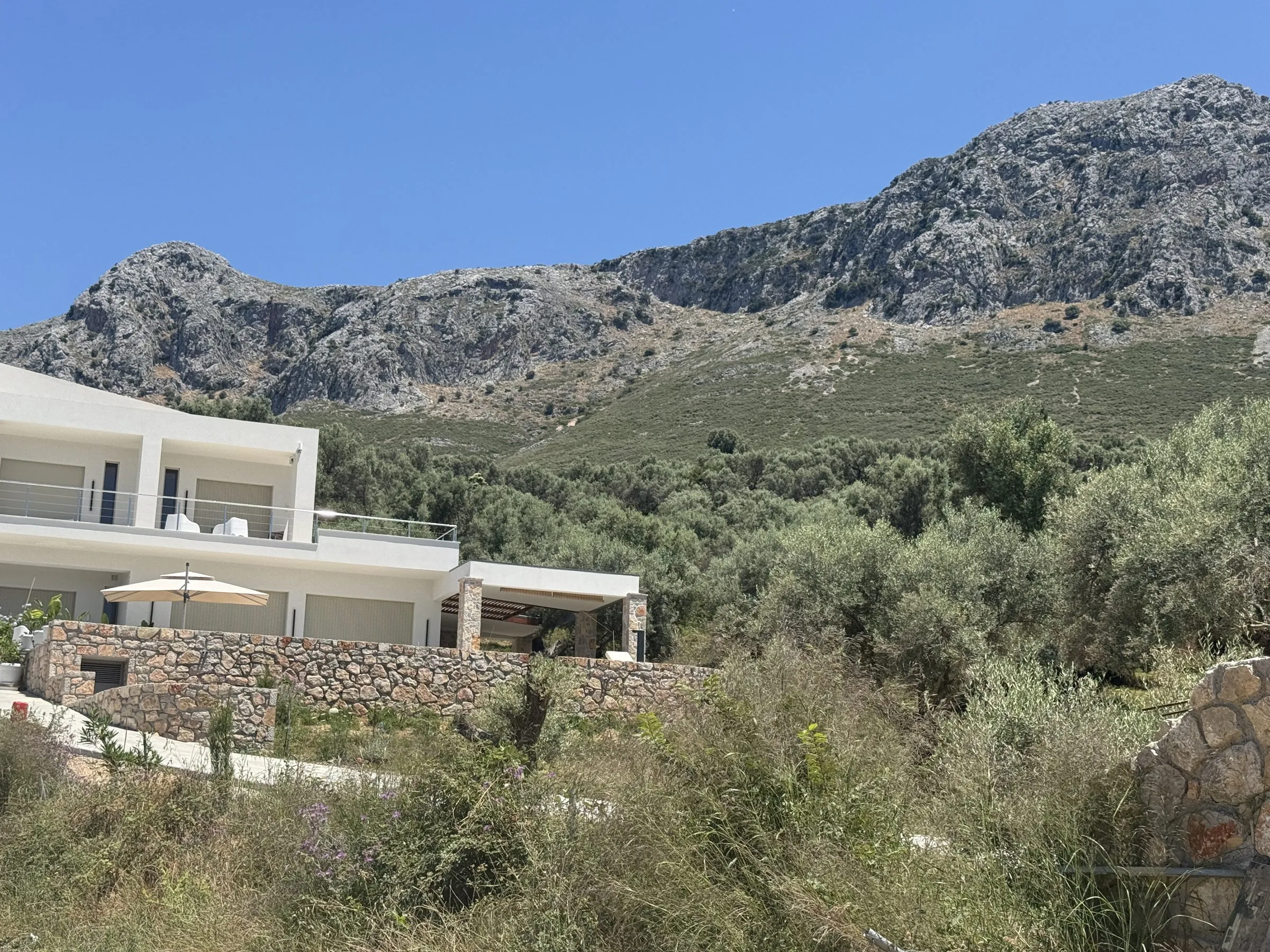 Exterior of Villa Prima, a modern white villa with stone terraces, set below the limestone mountains above Paleros.