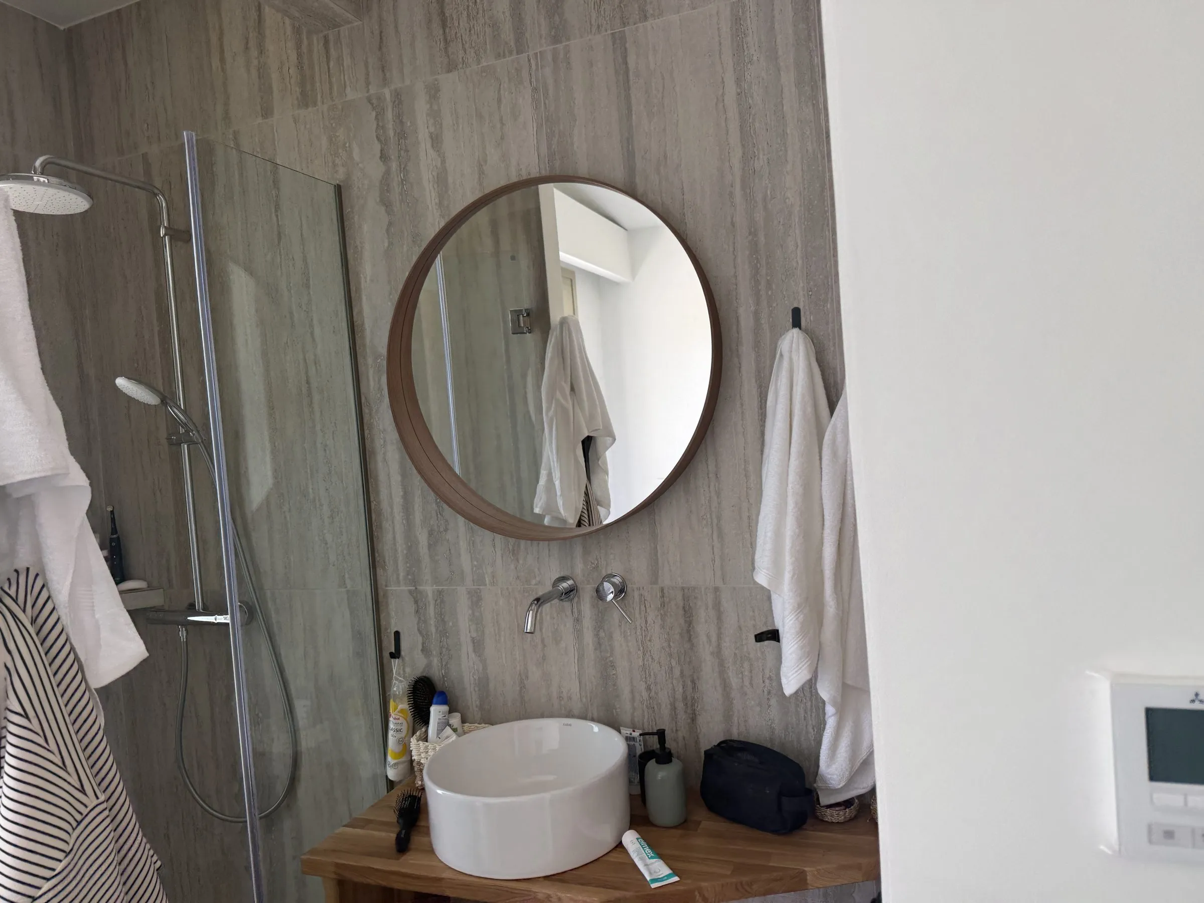 En-suite vanity at Villa Prima with a round wood-framed mirror, ceramic vessel basin and a glass walk-in shower.