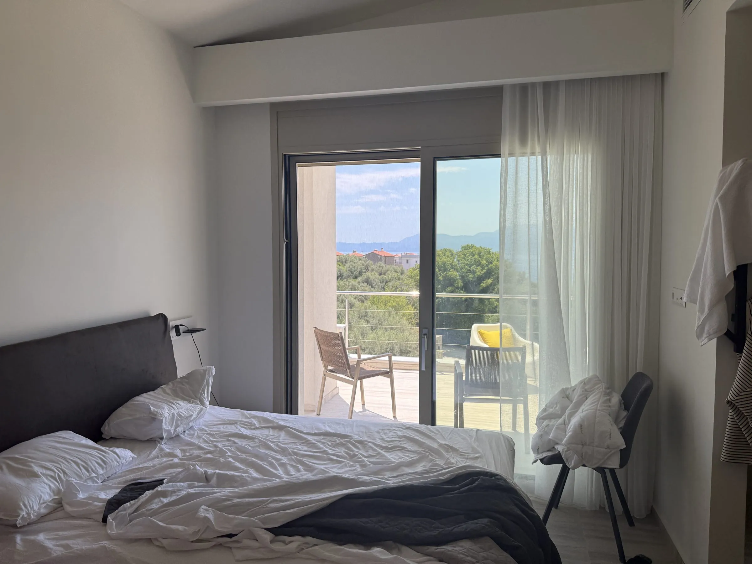 Double bedroom at Villa Prima with sliding doors onto a private balcony and views over the trees to the sea and mountains.