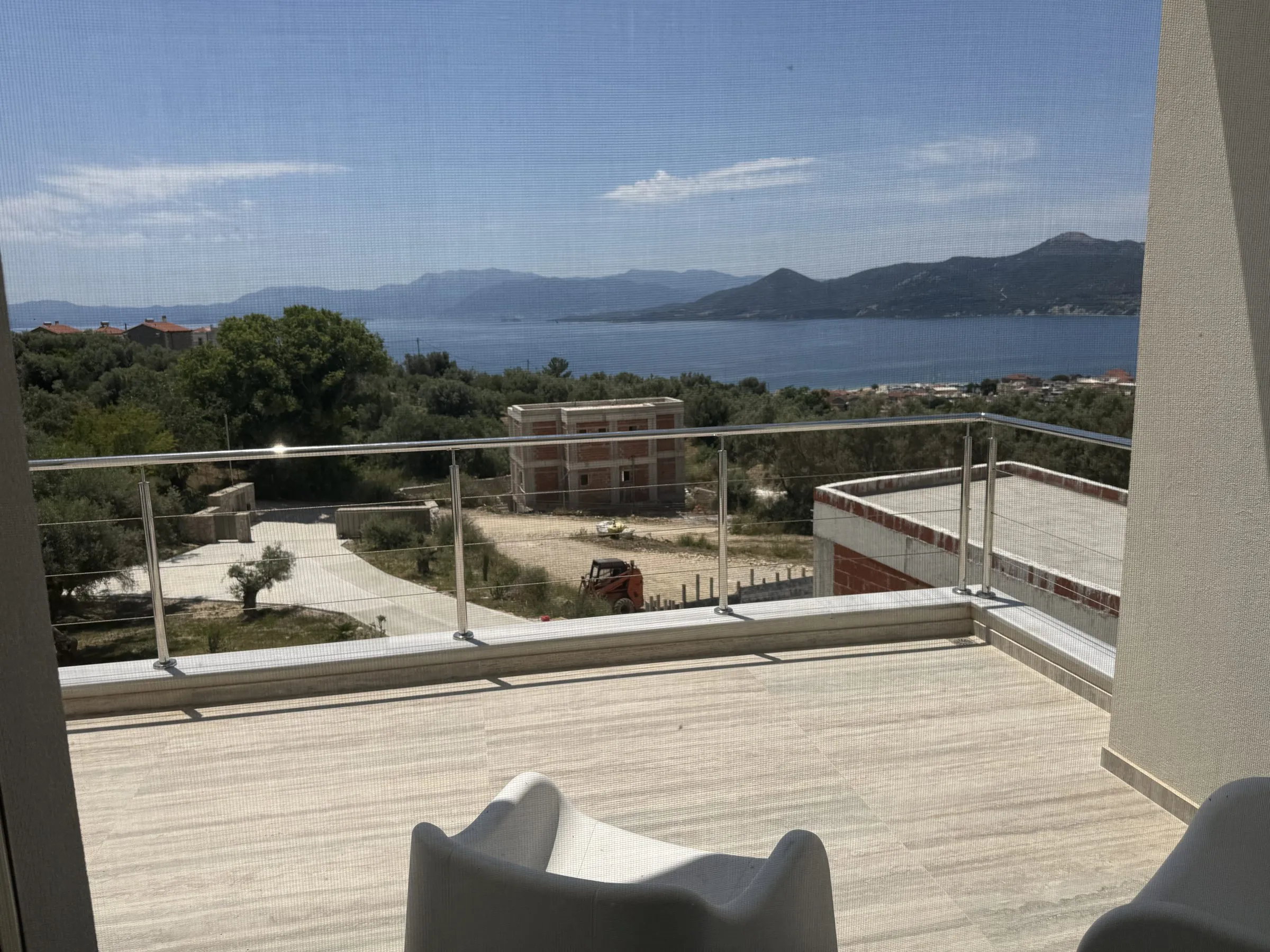 Spacious travertine terrace at Villa Prima with a glass balustrade and sweeping views over olive groves to the bay.