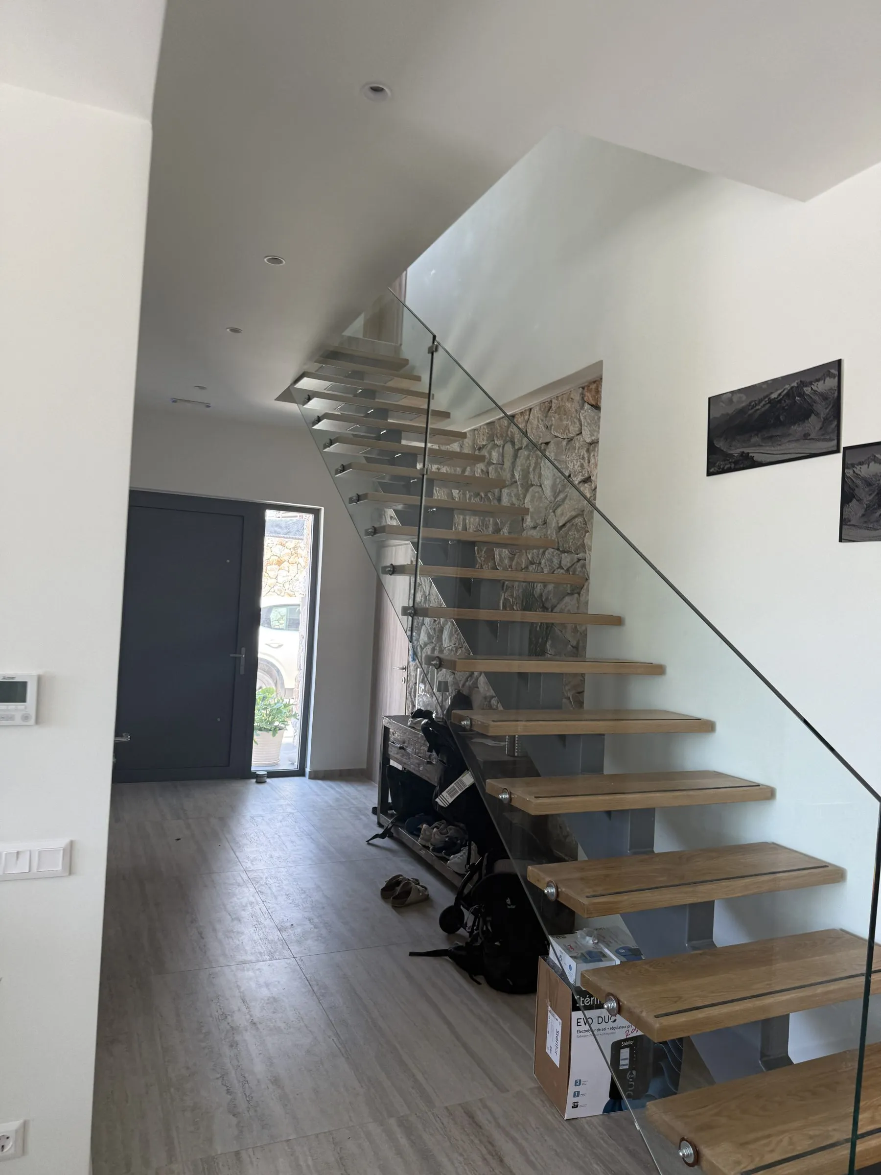 Entrance hall at Villa Prima with an open-tread oak-and-glass floating staircase against a natural stone feature wall.