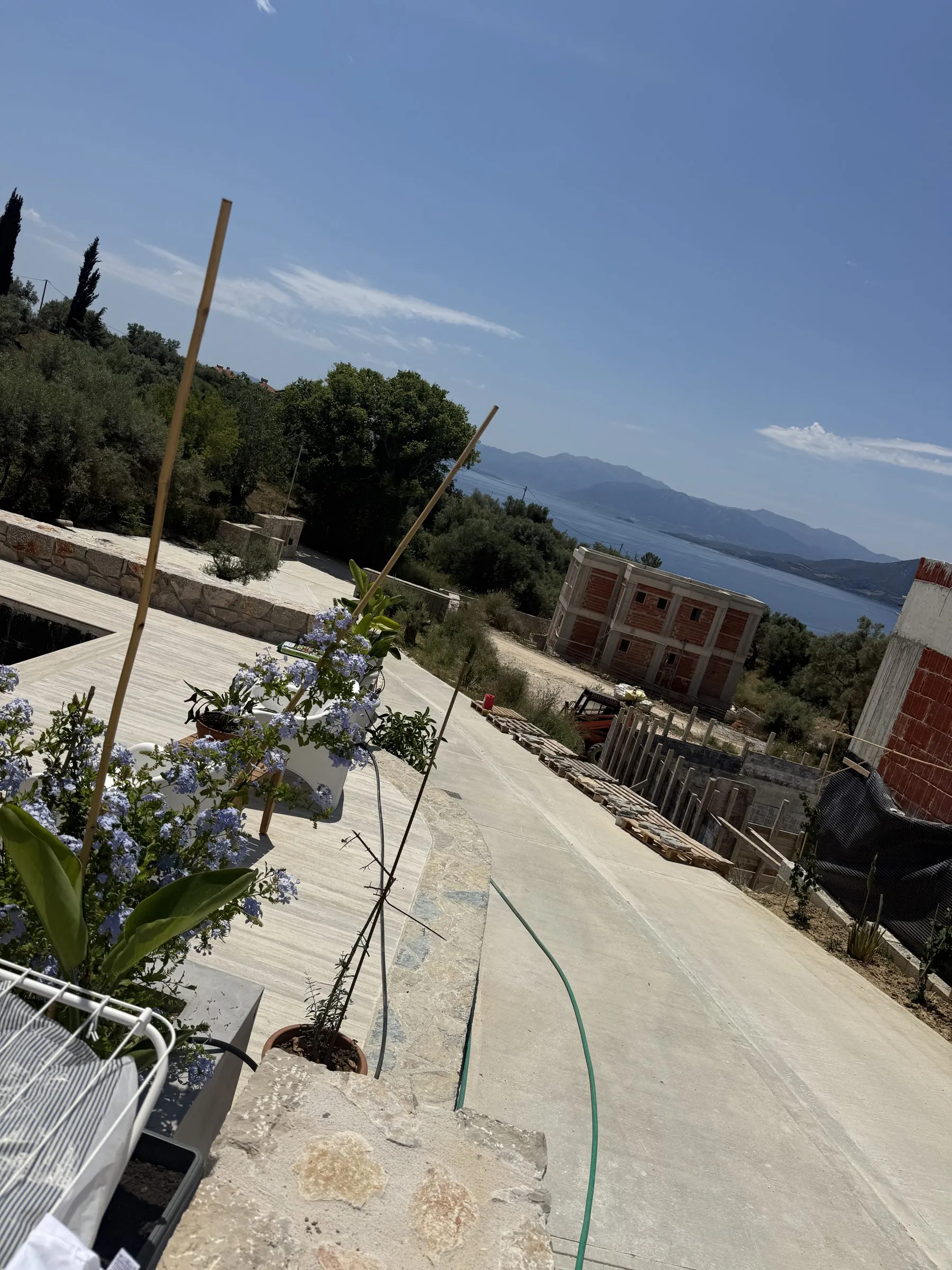 Planted terrace at Villa Prima with blue plumbago flowers and potted shrubs, looking out over the bay.